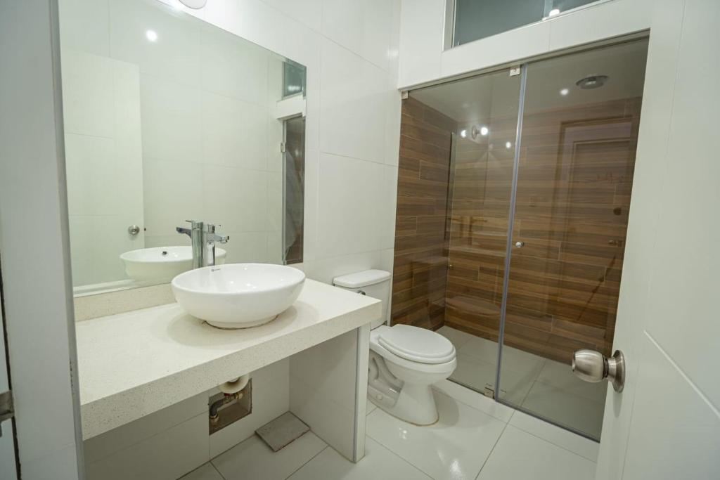 Baño con lavabo de cerámica blanca, espejo grande y ducha con mampara de vidrio