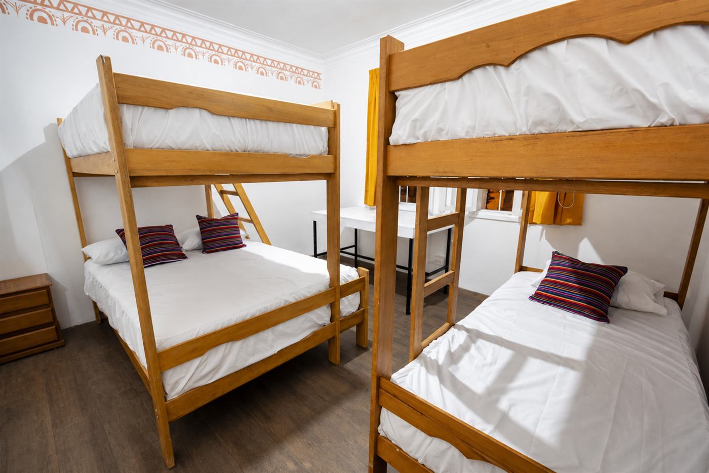 Dormitorio con dos literas de madera, ropa de cama blanca y cojines de colores